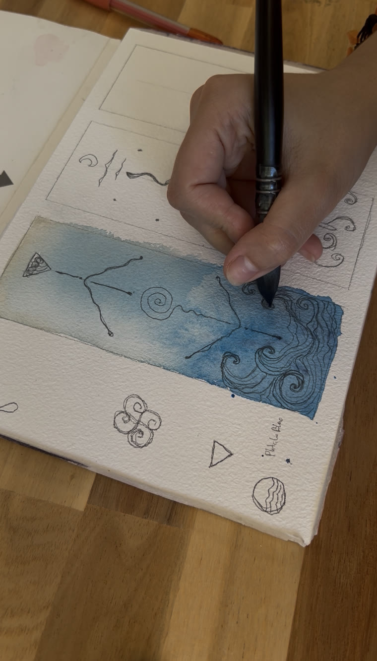 A hand inking wave lines over an indigo watercolour wash in a sketchbook